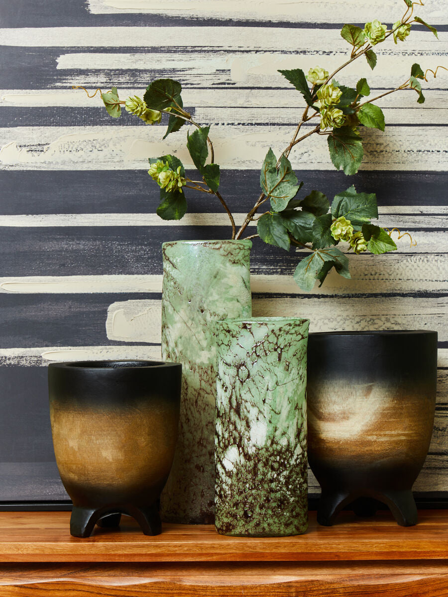 Three ceramic vases with greenery against a striped wall.