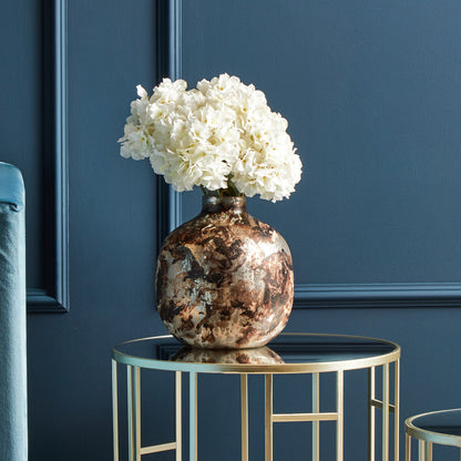Decorative vase with white flowers on a small round table against a blue wall.