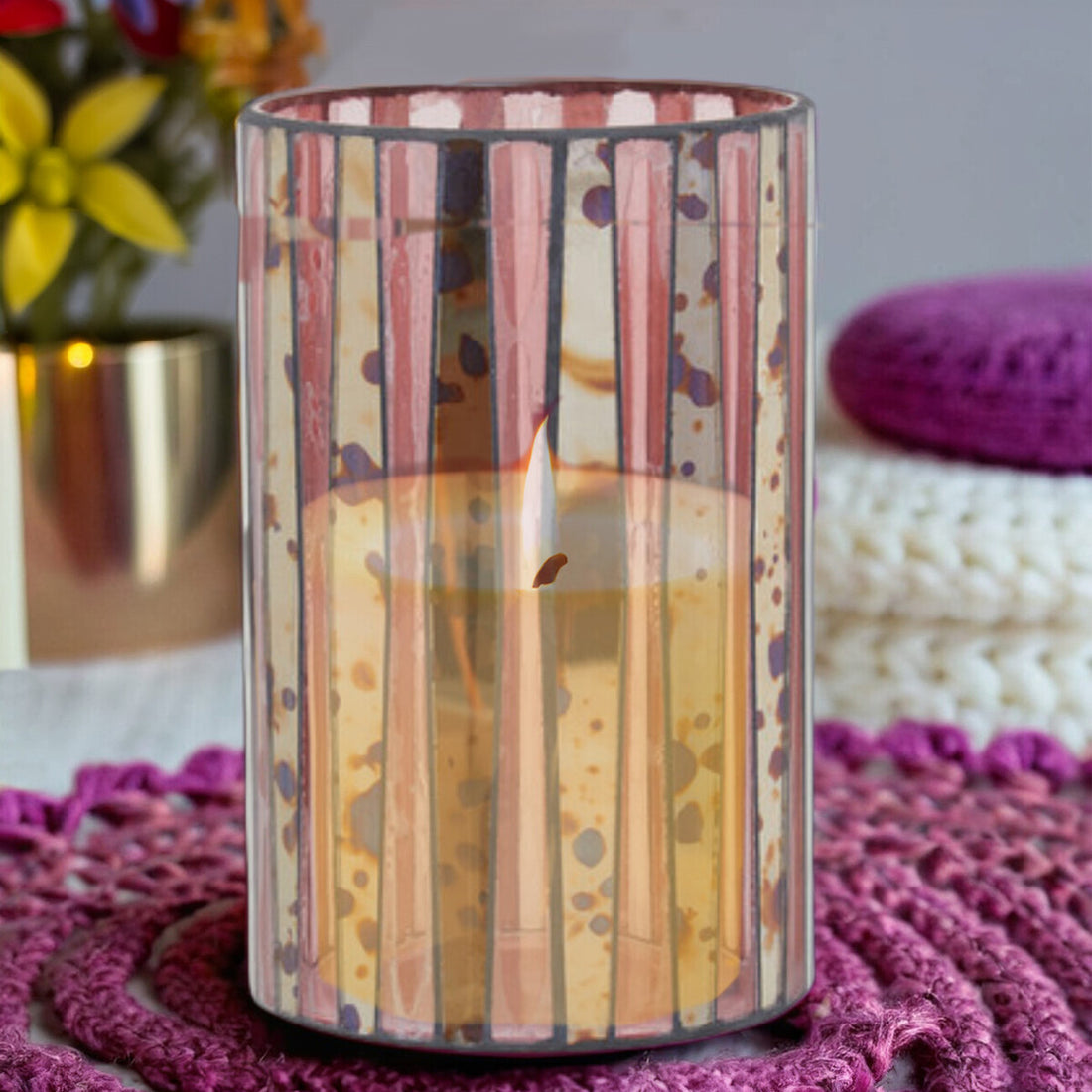 Decorative candle in a striped holder on a textured surface with flowers and a pillow in the background.