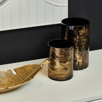 Decorative vases and a leaf-shaped tray on a white surface with a black wall background.