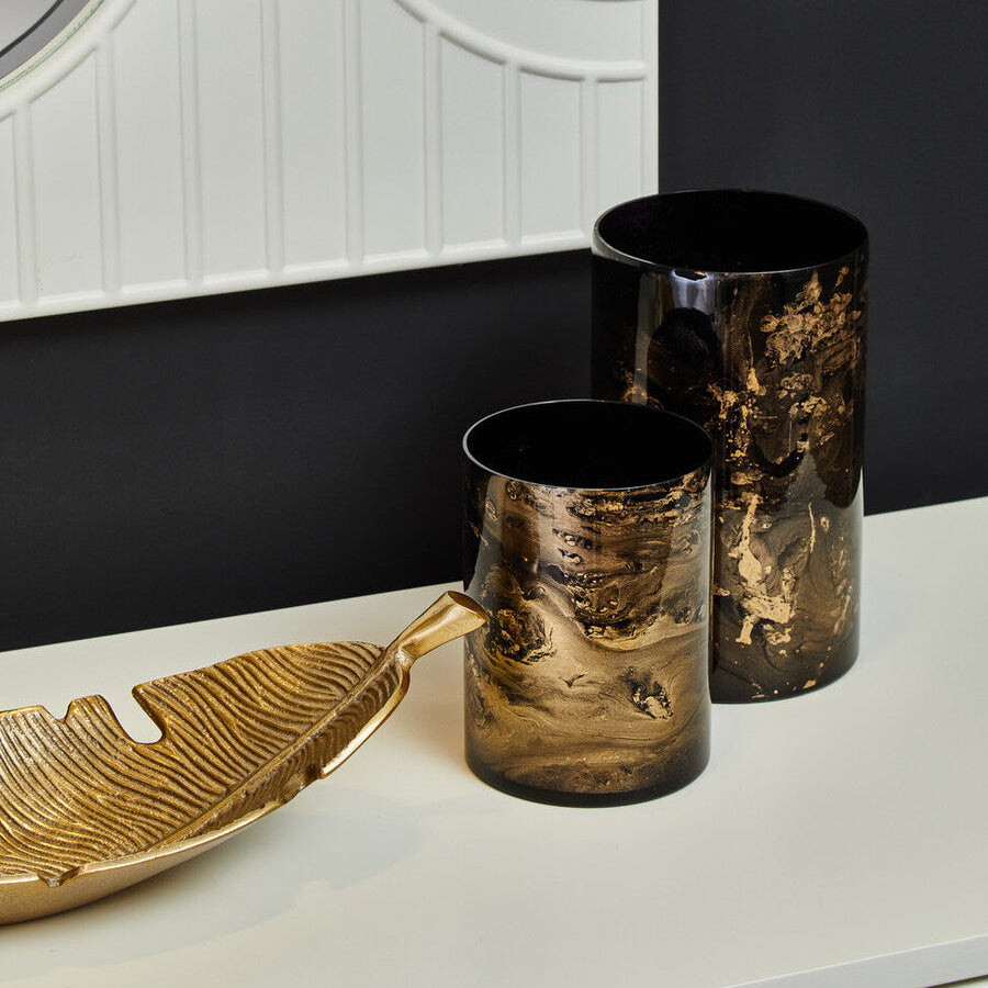 Decorative vases and a leaf-shaped tray on a white surface with a black wall background.