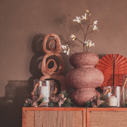 Decorative setting with a textured vase, wooden sculpture, and other items on a wicker cabinet.