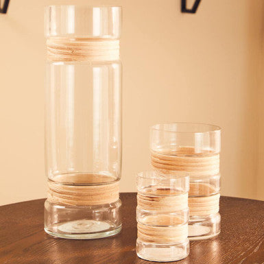 Two glass vases with wooden accents on a wooden surface against a beige wall.