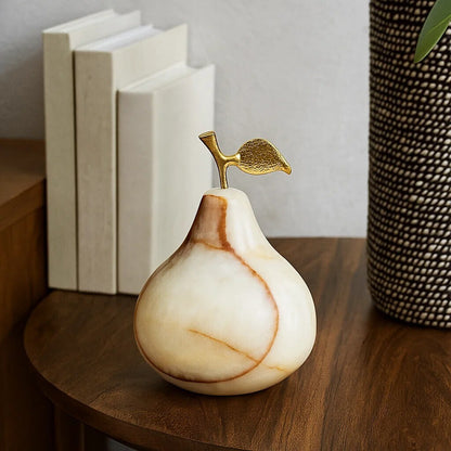 Decorative marble pear with gold leaf on a wooden surface with books and a textured vase in the background.