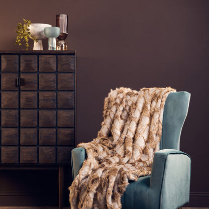 Blue armchair with a fur throw blanket in a room with a dark brown wall and wooden floor.