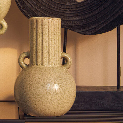Two beige vases on a reflective surface with a textured wall in the background