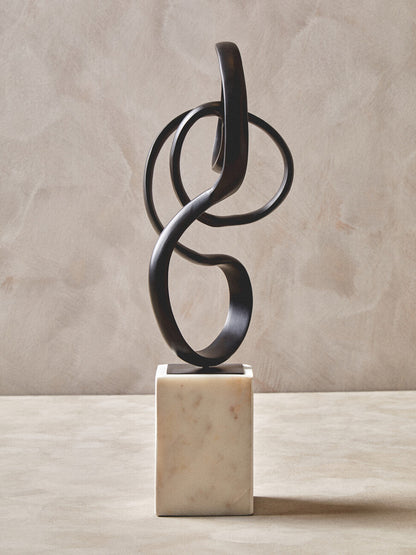 Abstract metal sculpture on a marble base against a beige background