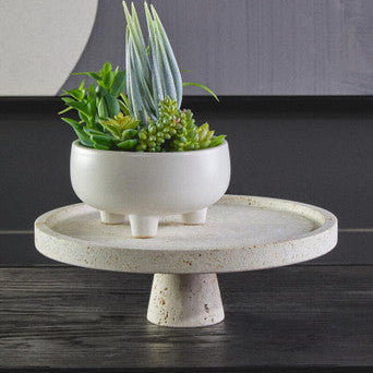 Decorative plant stand with a small potted plant on a dark surface