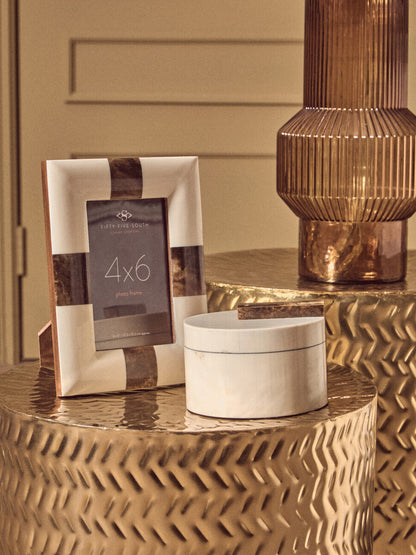 Decorative items including a photo frame and a small round container on a gold surface.