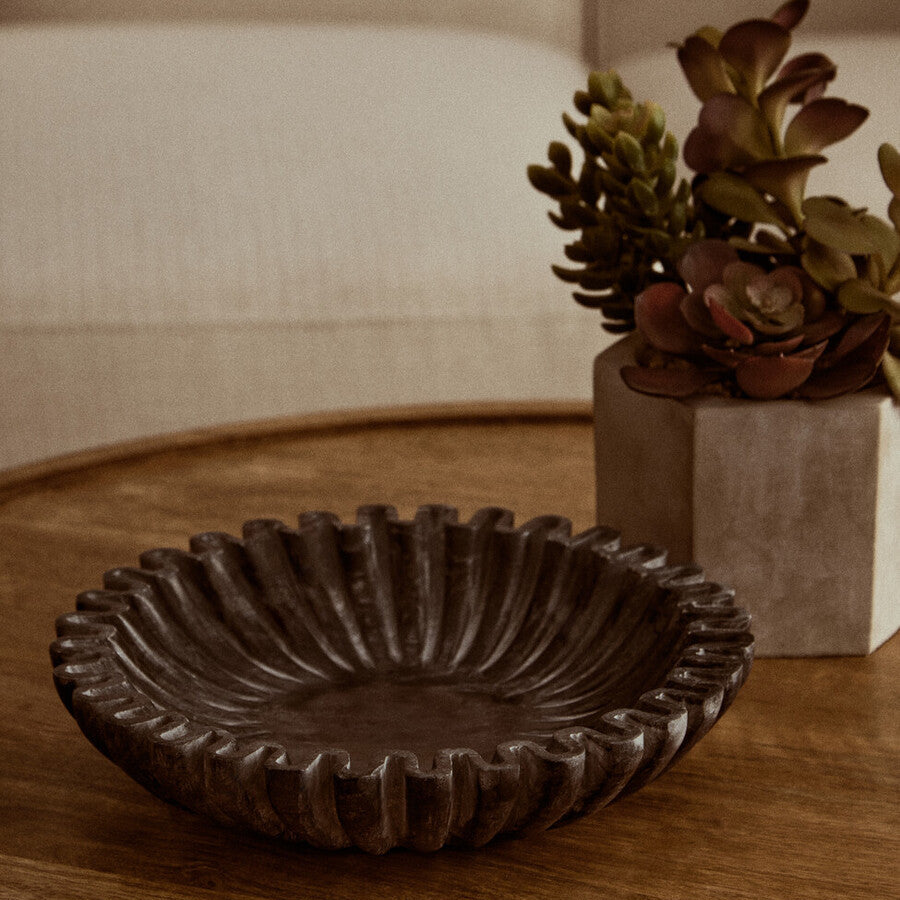 Decorative brown ceramic bowl on a wooden surface with a plant in the background