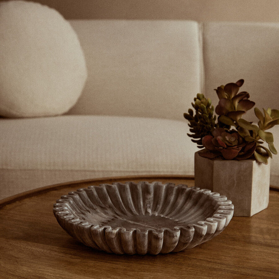 Decorative bowl on a wooden coffee table with a beige sofa and plant in the background