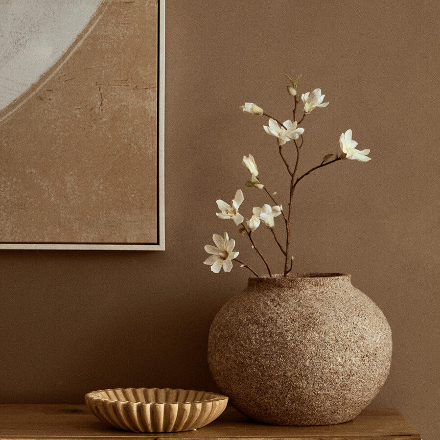 Decorative vase with white flowers on a wooden cabinet against a brown wall.