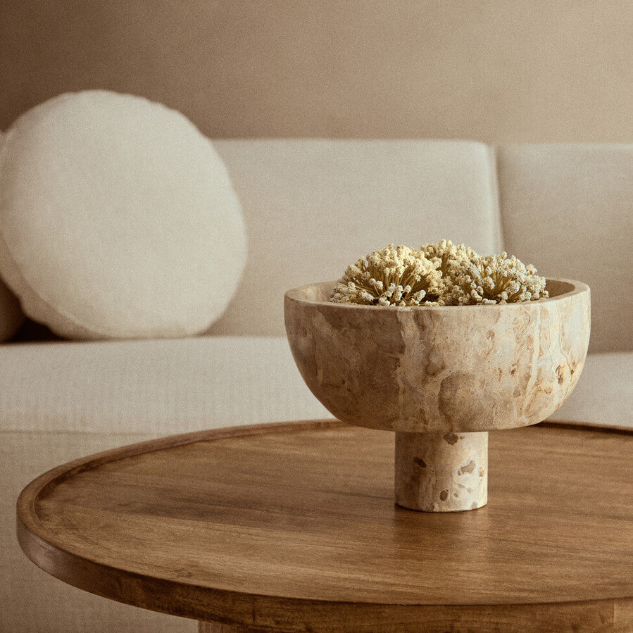 Wooden table with a decorative bowl containing flowers, placed in a living room setting.