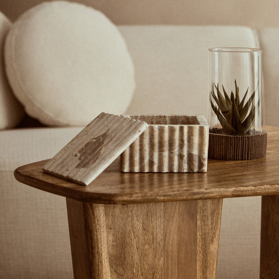 Wooden side table with decorative items including a striped box, glass container with plant, and spherical object.