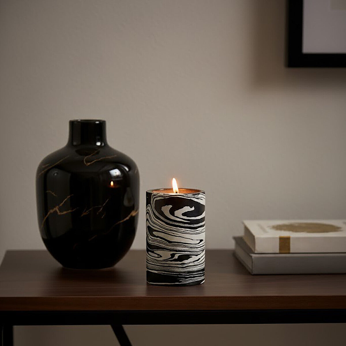 Black vase and marbled candle on a wooden surface with a neutral background