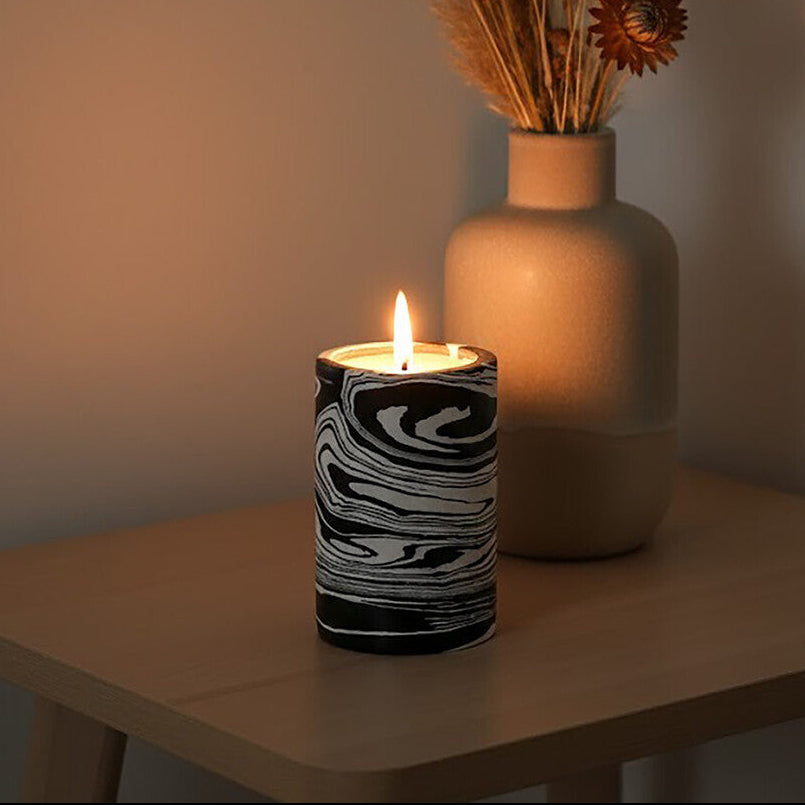 Candle with black and white pattern and a vase with dried flowers on a wooden table.