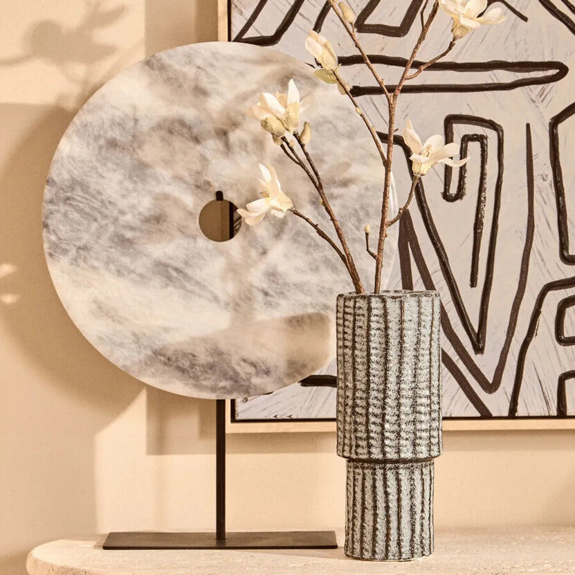 Decorative setup with a marble-patterned lamp, vase with branches, and abstract wall art.