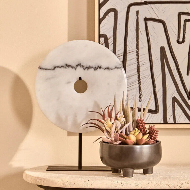 Decorative setup with a marble sphere, plant in a pot, and abstract art on a beige wall.