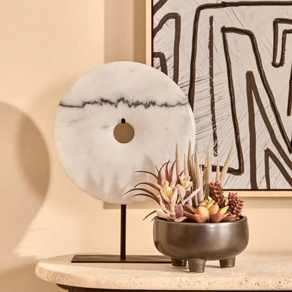 Decorative setup with a marble sphere, plant in a pot, and abstract art on a beige wall.