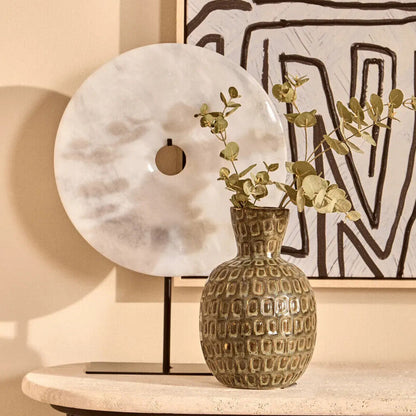 Decorative vase with greenery on a table against a wall with abstract art