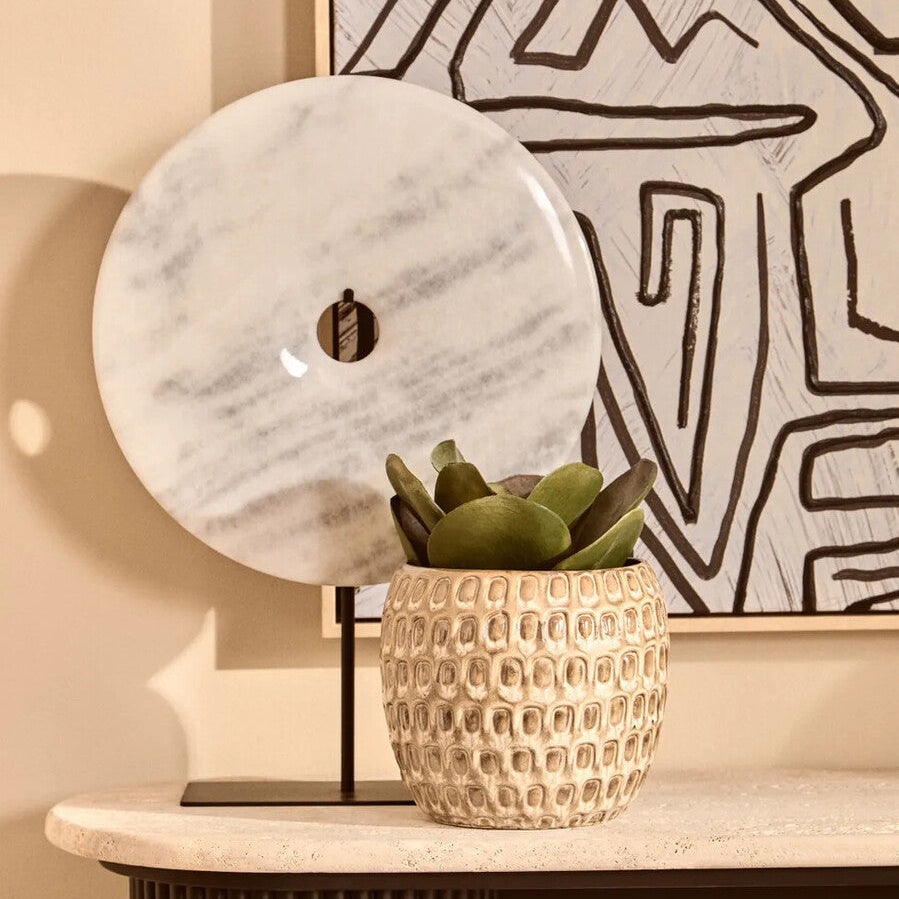 Decorative scene with a textured vase, marble orb, and abstract art on a wall.
