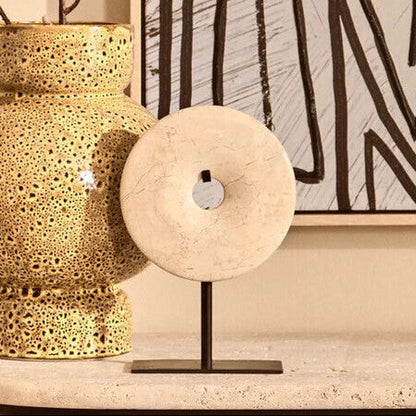Decorative gold vase with floral arrangement on a table next to abstract art.