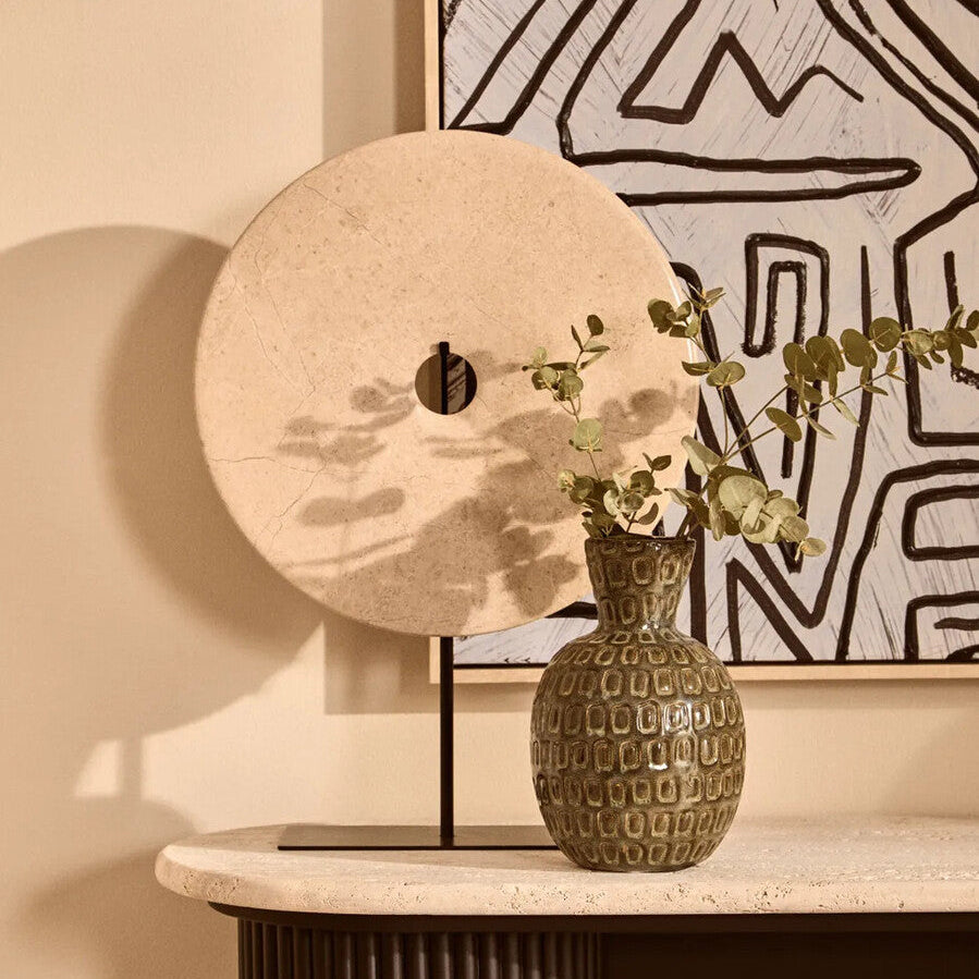 Decorative vase with greenery on a table against a wall with abstract art