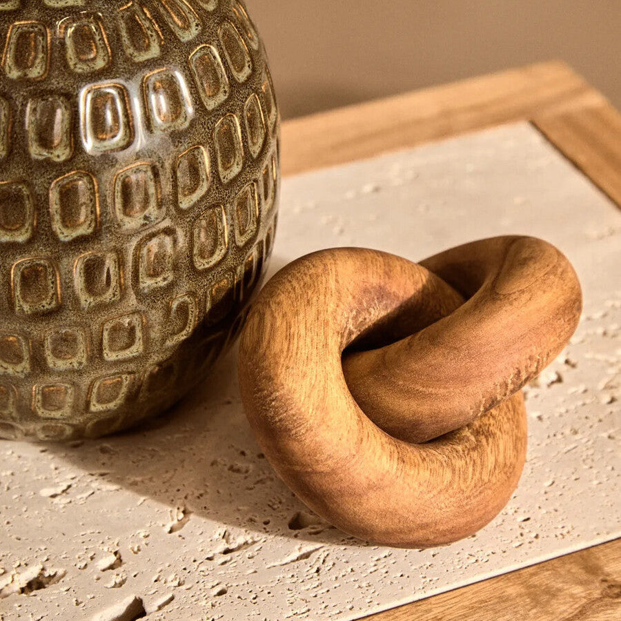 Wooden knot sculpture next to a textured ceramic vase on a wooden surface.
