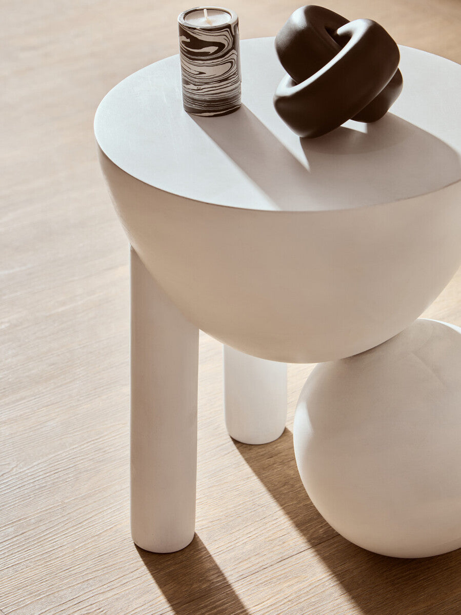 White side table with a candle and decorative object on a wooden floor