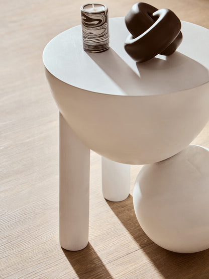 White side table with a candle and decorative object on a wooden floor