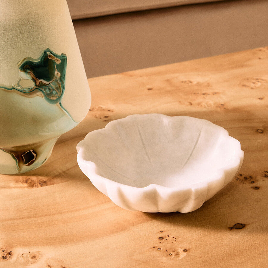 White ceramic bowl on a wooden surface with a blurred green vase in the background