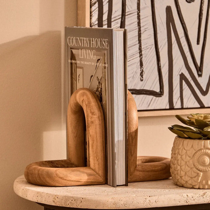 Wooden bookends holding a magazine on a shelf with abstract art in the background