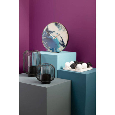 Decorative items including a round mirror, black candle holders, and white eggs against a purple wall.