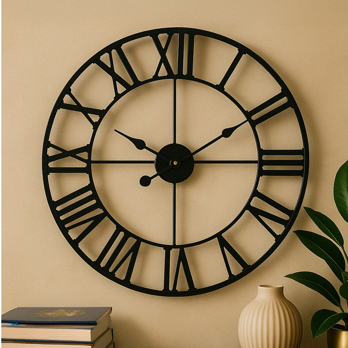 Large black wall clock with Roman numerals on a beige wall, next to a vase and books.