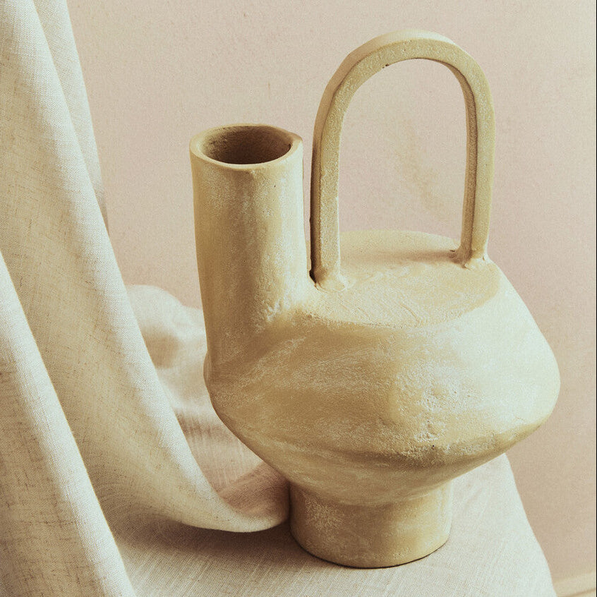 Beige ceramic vase with a handle on a light fabric surface with a soft pink background
