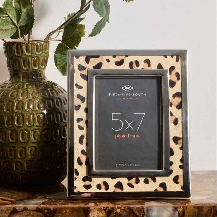 Leopard print photo frame with a 5x7 size label next to a textured green vase on a marble surface.