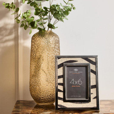 Decorative vase with greenery and a photo frame on a wooden surface.