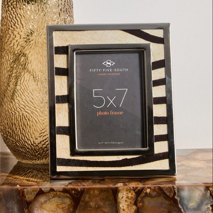 5x7 photo frame with zebra pattern on a decorative shelf next to a textured vase with greenery.