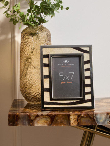 Decorative photo frame with zebra pattern on a marble surface next to a textured vase with greenery.