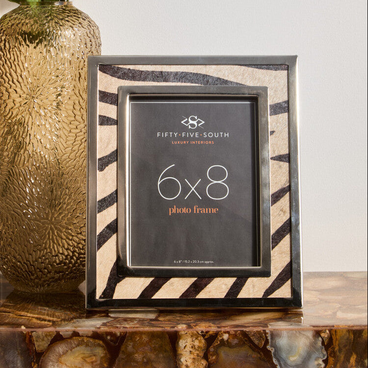 Decorative photo frame with striped design next to a textured vase on a table.