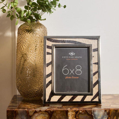 Decorative photo frame with striped design on a wooden surface next to a textured vase.