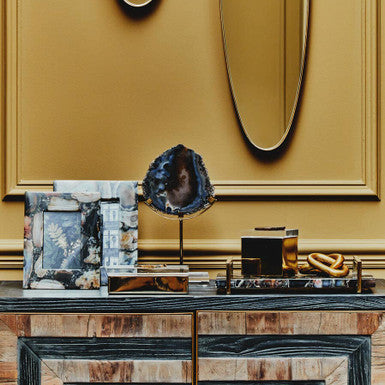 Decorative console table with a gold wall and abstract art in a stylish interior setting.