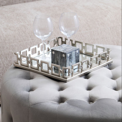 Gray tufted ottoman with a decorative tray and glasses on top, against a neutral background.