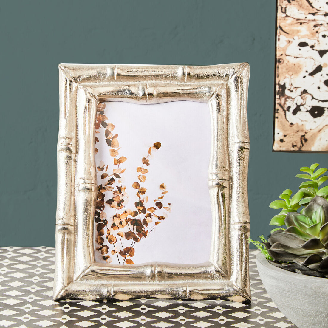 Decorative silver frame with a floral design on a patterned surface.