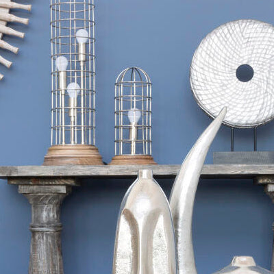 Decorative setting with metallic sculptures, a round mirror, and striped candlesticks against a blue wall.