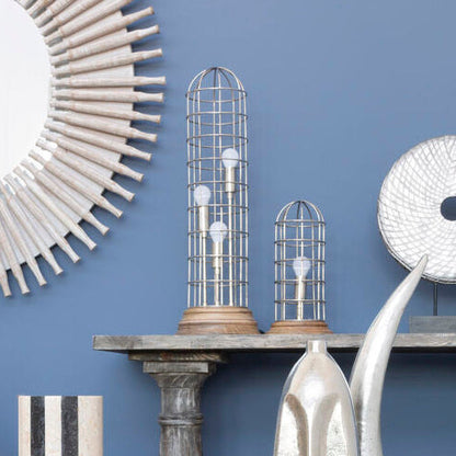 Decorative setting with metallic sculptures, a round mirror, and striped candlesticks against a blue wall.