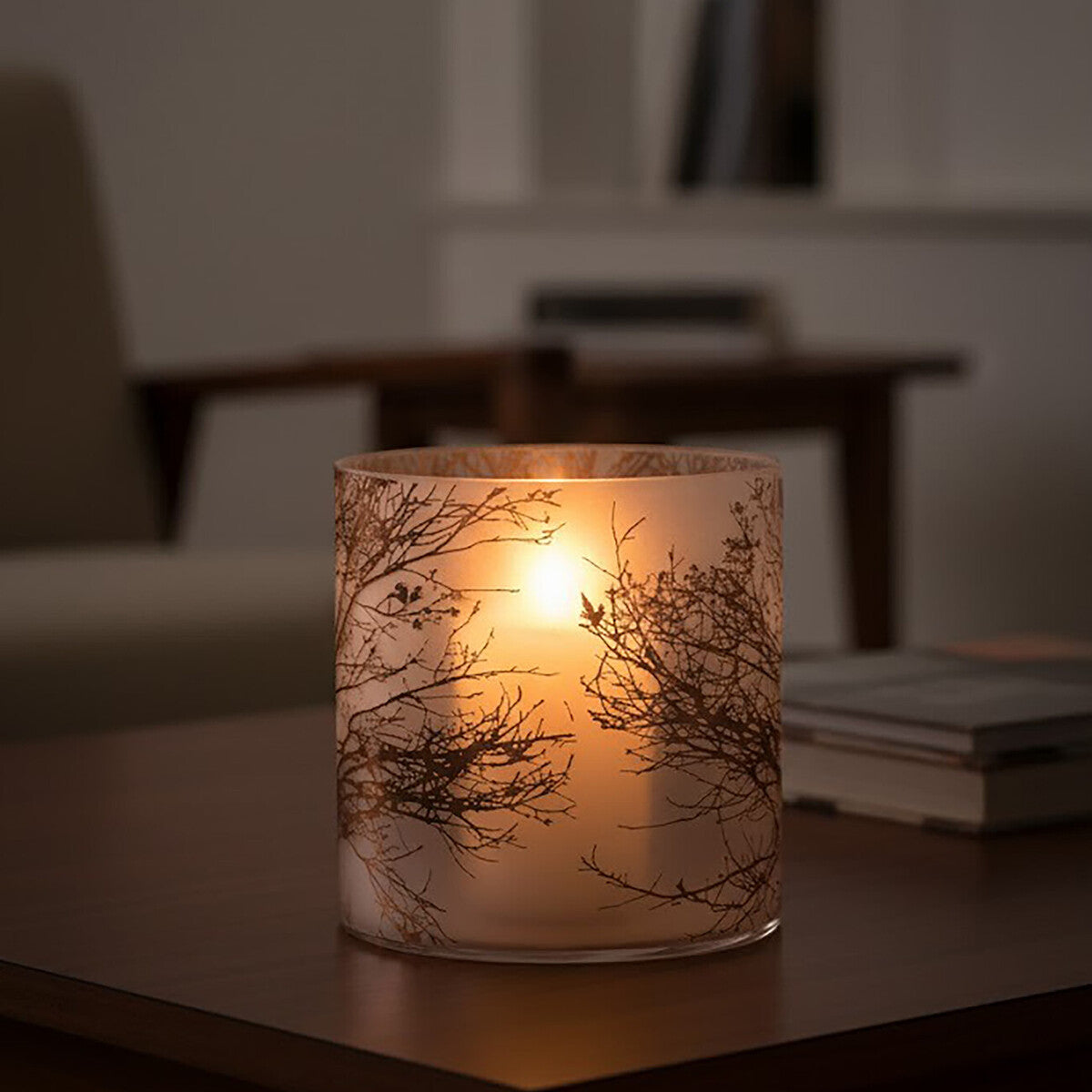 Candle in a decorative holder with tree design on a table in a dimly lit room.