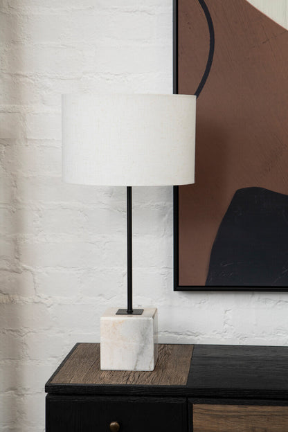 Modern lamp with marble base on a wooden side table against a white brick wall.