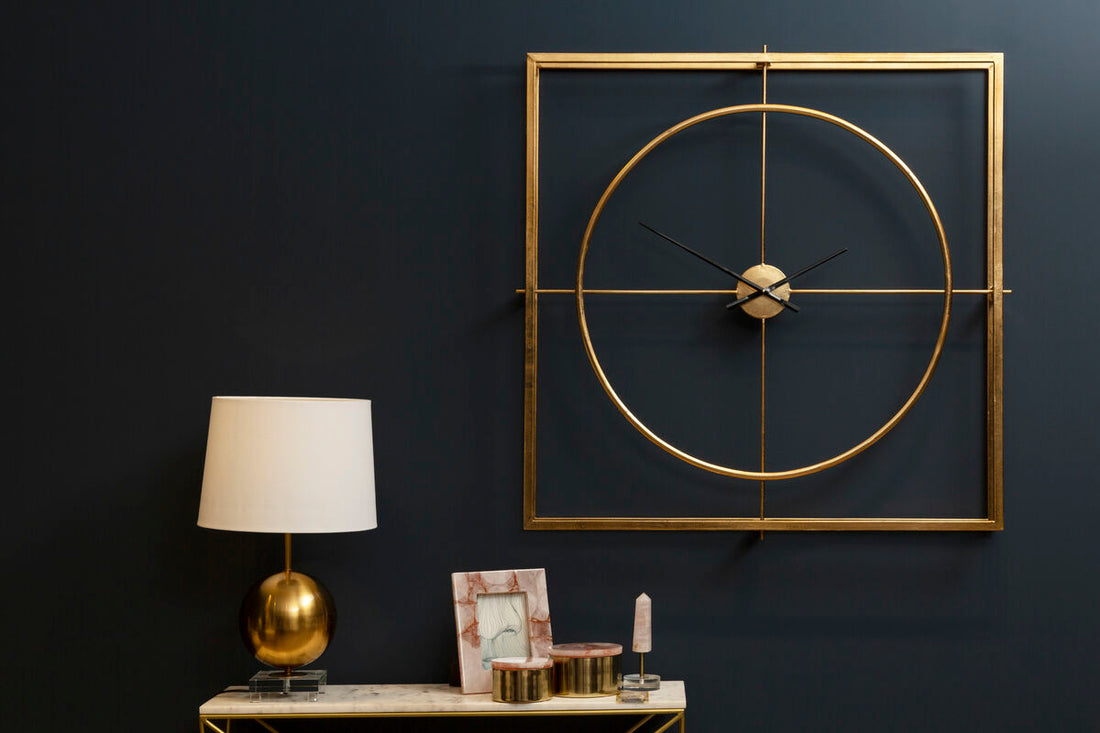 Gold wall clock on a dark wall with a lamp and decorative items on a table.