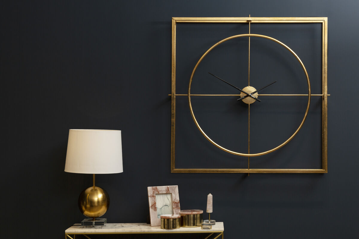 Gold wall clock on a dark wall with a lamp and decorative items on a table.